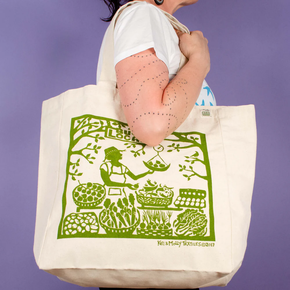 Person holding a tote bag with green printed design against a purple background