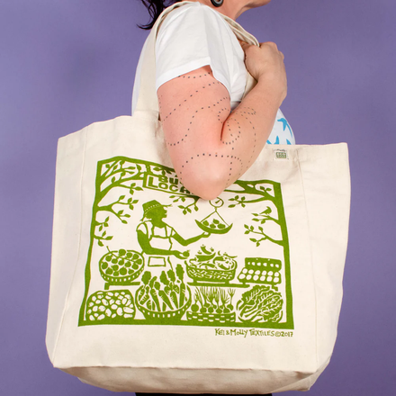 Person holding a tote bag with green printed design against a purple background