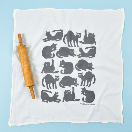 White towel with gray cat pattern and wooden rolling pin on a light blue background
