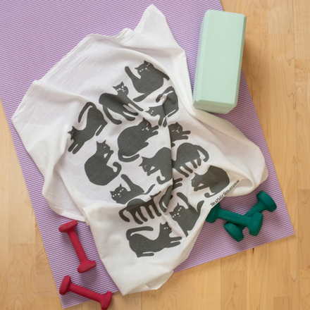 White towel with grey cat pattern on a purple mat with exercise equipment.