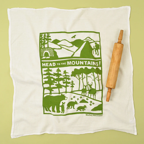 Cotton tea towel with mountain design and rolling pin on a green background