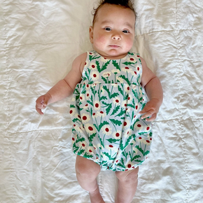 Baby wearing a floral romper lying on a white bed