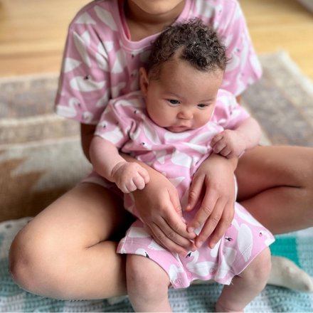 Two children in matching pink outfits sitting on a rug.