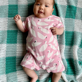 Baby in a pink onesie with white patterns lying on a green and white checkered blanket