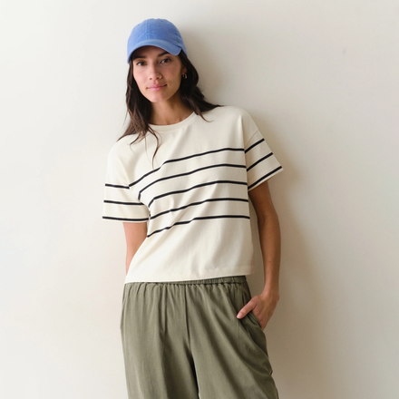 Woman wearing a white shirt with black stripes and green pants on a neutral background.