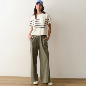 Woman wearing a white shirt with black stripes and green pants on a neutral background.