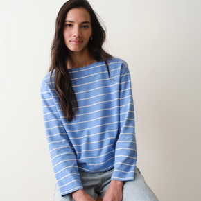 Woman wearing a blue striped long sleeved tee sitting on a chair against a plain background