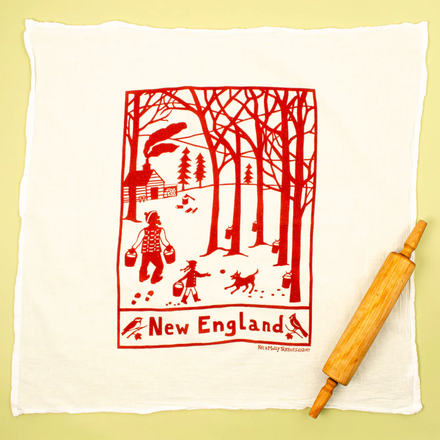 White towel with red New England scene design and wooden rolling pin on a yellow background